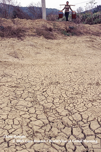 Chinese woman in northern Guangdong Province carries water past dry fish pond in a severe drought