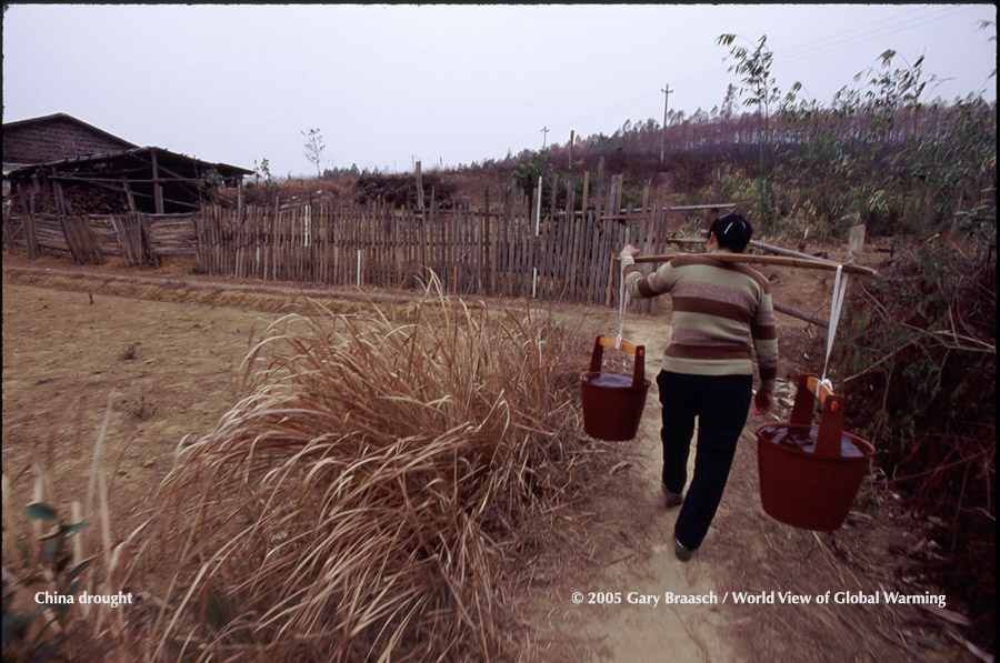 Chinese woman in northern Guangdong Province carries water past dry fish pond in a severe drought. January 2005.